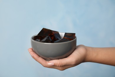 Photo of Woman holding bowl with delicious grass jelly cubes on light blue background, closeup