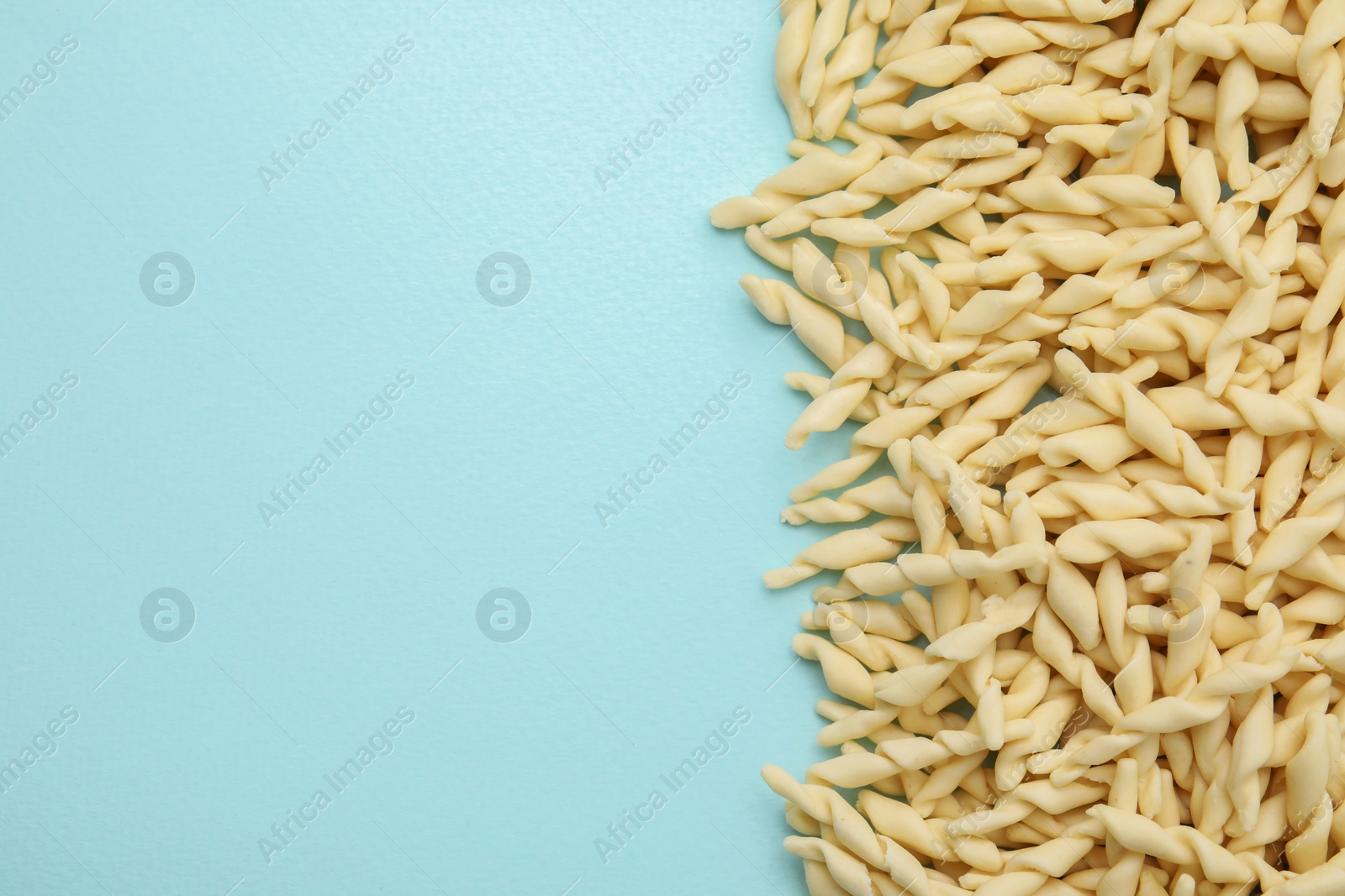 Photo of Uncooked trofie pasta on light blue background, flat lay. Space for text