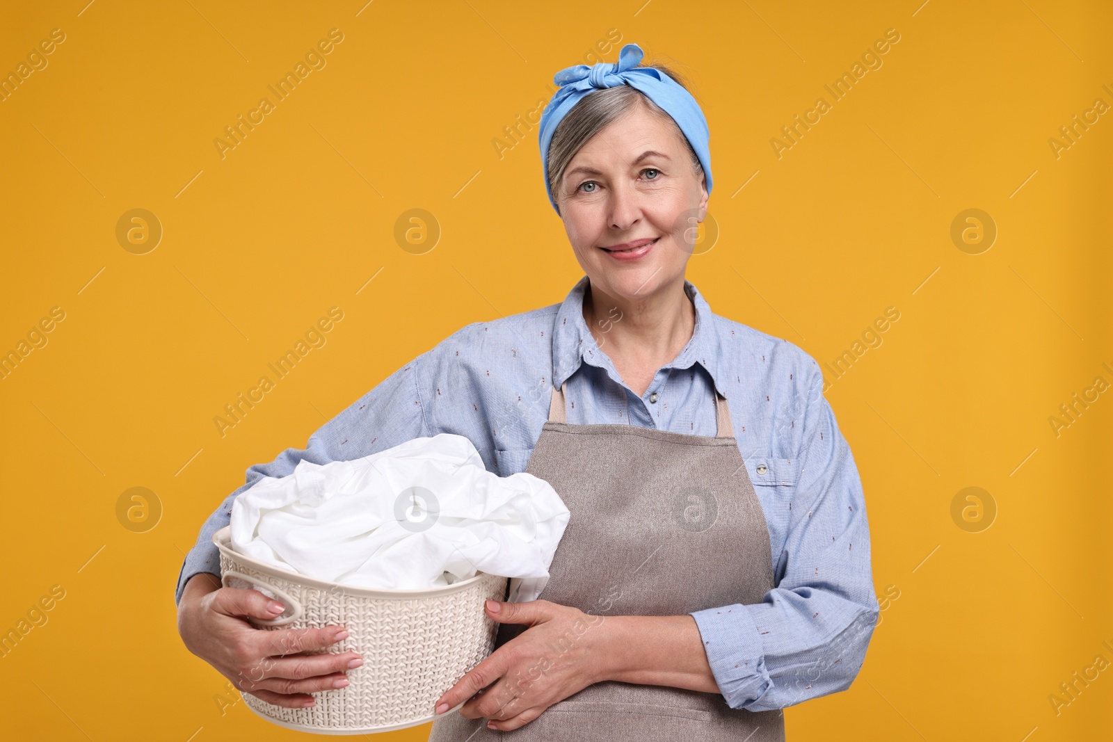 Photo of Happy housewife with basket full of laundry on orange background