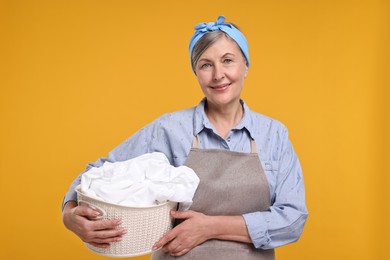 Happy housewife with basket full of laundry on orange background