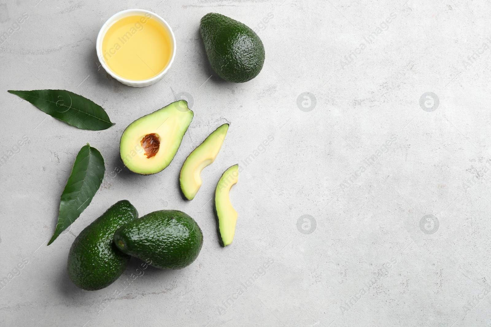 Photo of Bowl of natural oil and avocados on grey stone background, flat lay. Space for text