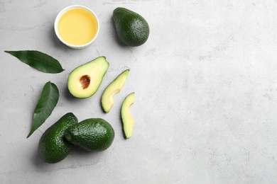 Bowl of natural oil and avocados on grey stone background, flat lay. Space for text