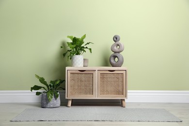Photo of Wooden chest of drawers with decor and houseplants near light green wall indoors