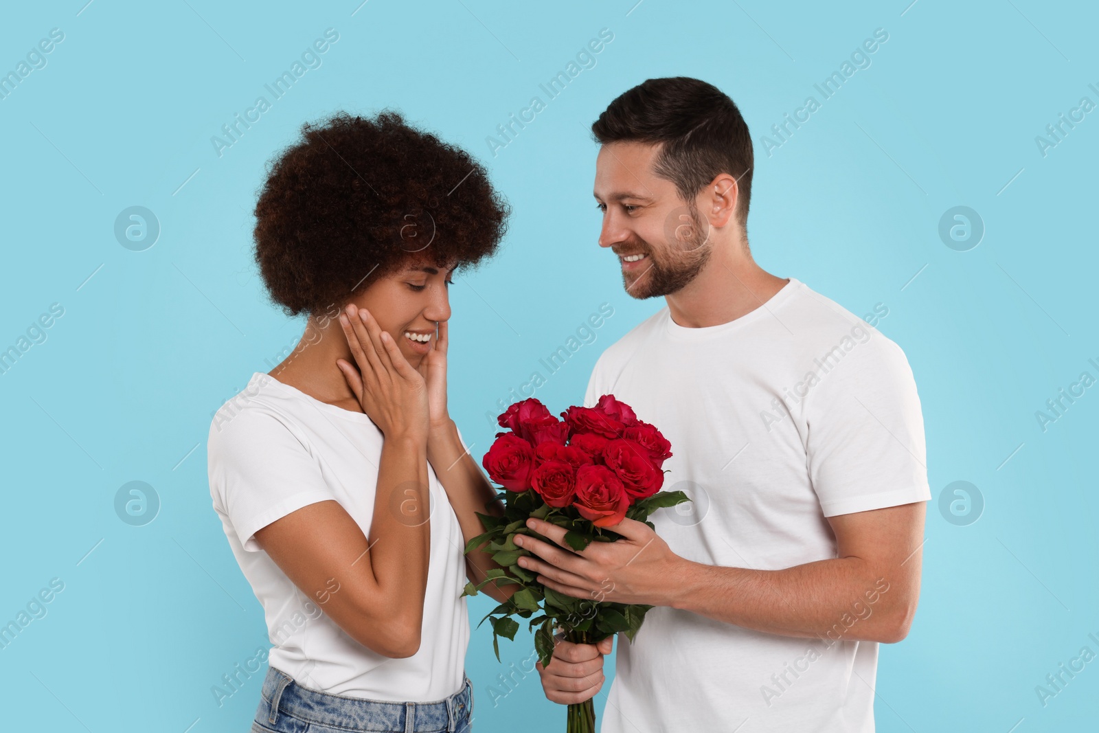 Photo of International dating. Handsome man presenting roses to his beloved woman on light blue background