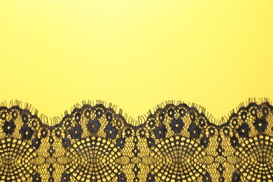 Photo of Black lace on yellow background, top view. Space for text