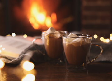Delicious sweet cocoa with marshmallows and blurred fireplace on background