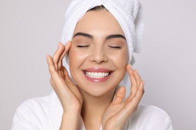 Young woman in bathrobe with towel on light grey background. Spa treatment