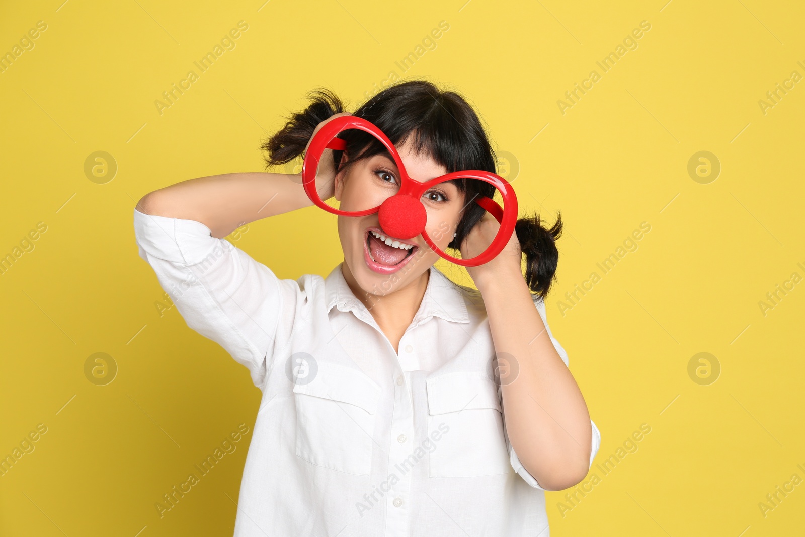 Photo of Funny woman with clown nose and large glasses on yellow background. April fool's day