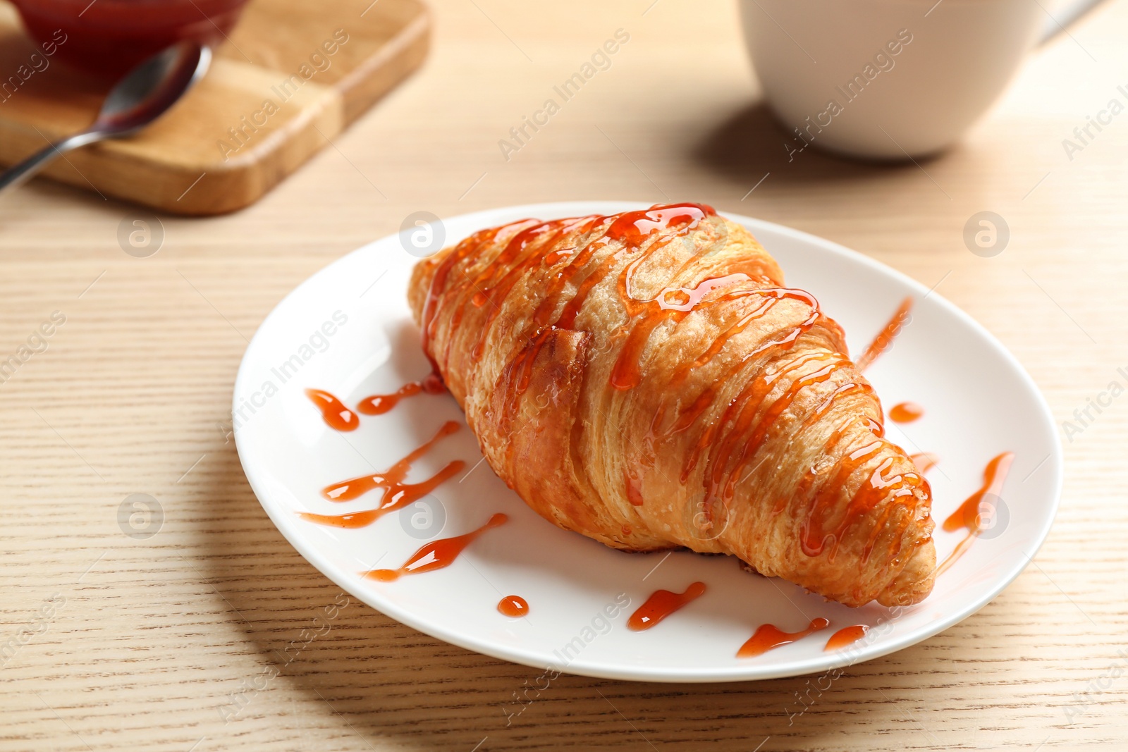 Photo of Plate of fresh croissant with jam on wooden table, closeup. French pastry