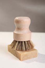 Photo of One cleaning brush and bar of soap on white textured table, closeup