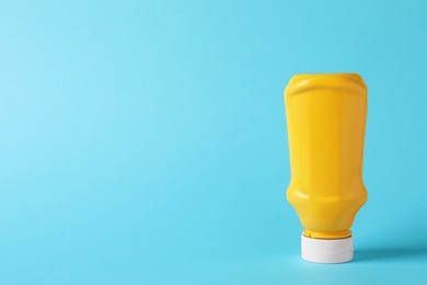 Photo of Spicy mustard in plastic bottle on light blue background, space for text