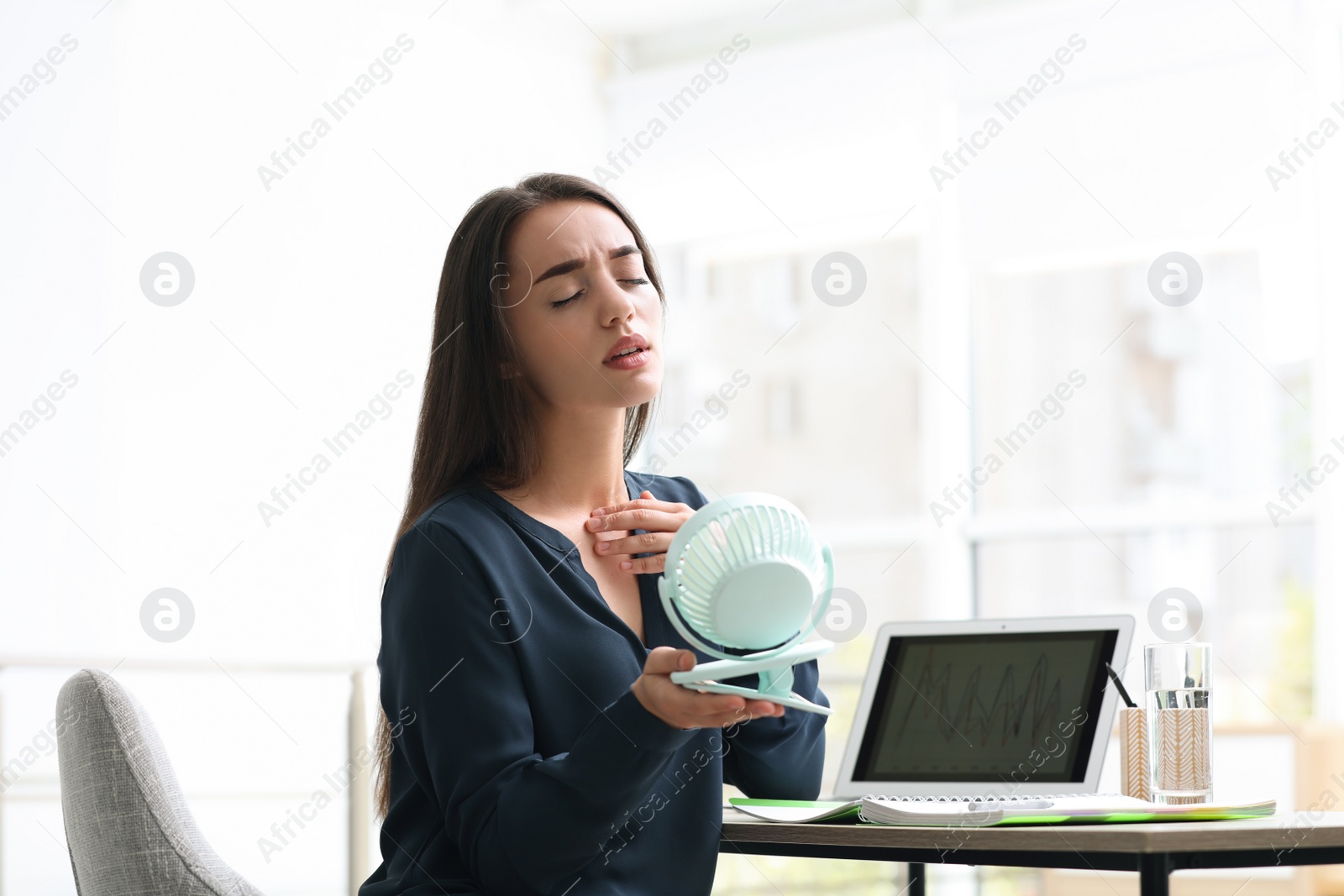 Photo of Woman with portable fan suffering from heat at workplace. Summer season