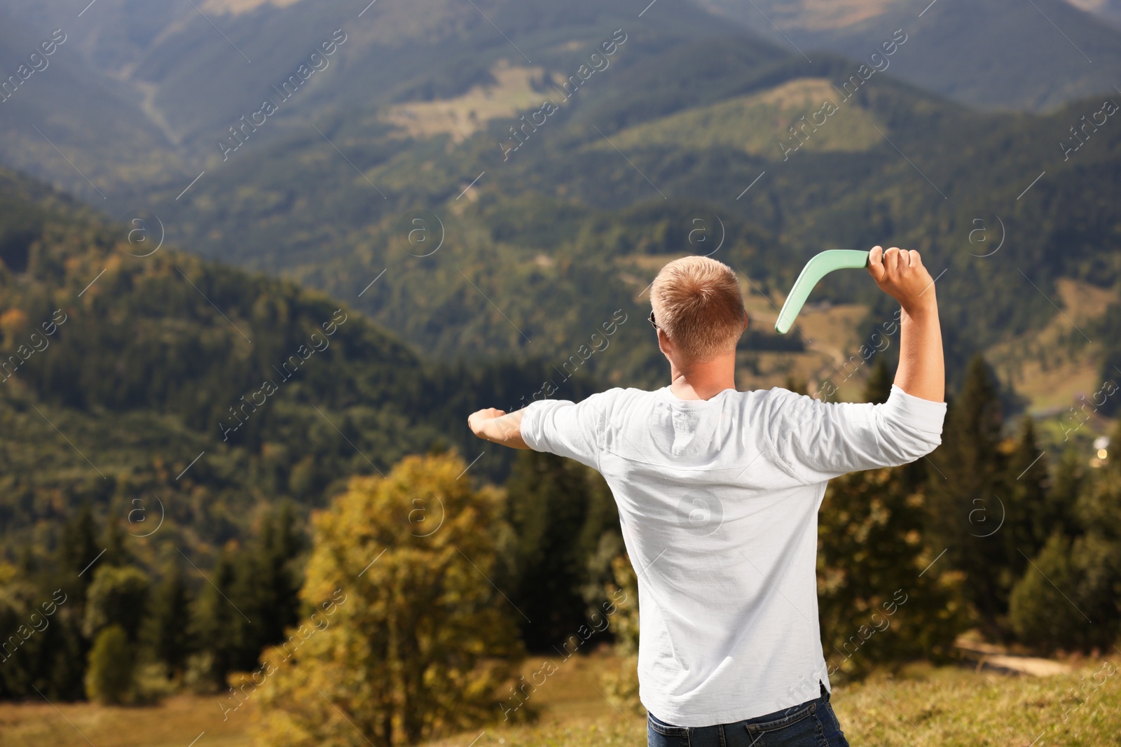 Photo of Man throwing boomerang in mountains on sunny day, back view. Space for text