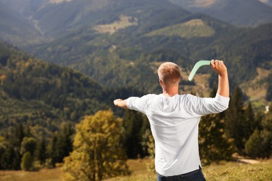 Man throwing boomerang in mountains on sunny day, back view. Space for text