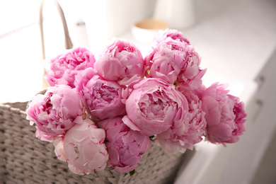 Photo of Basket with beautiful pink peonies in kitchen, closeup