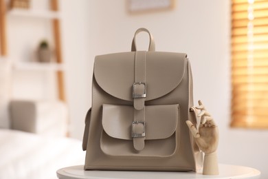 Photo of Stylish beige backpack and wooden mannequin hand on white table indoors