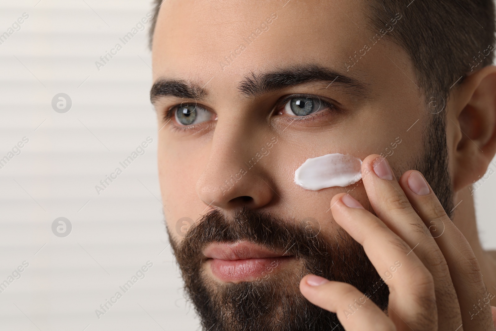 Photo of Man with dry skin applying cream onto his face on light background, closeup. Space for text