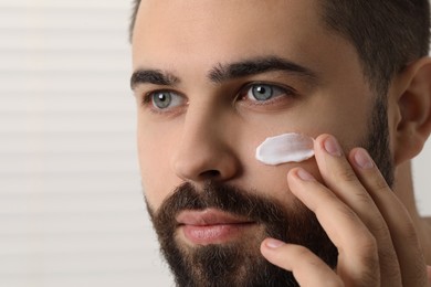 Photo of Man with dry skin applying cream onto his face on light background, closeup. Space for text