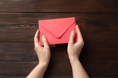 Woman with red paper envelope at wooden table, top view