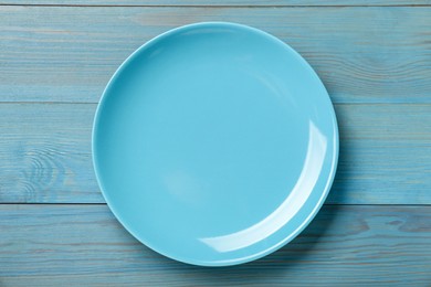 Empty ceramic plate on light blue wooden table, top view