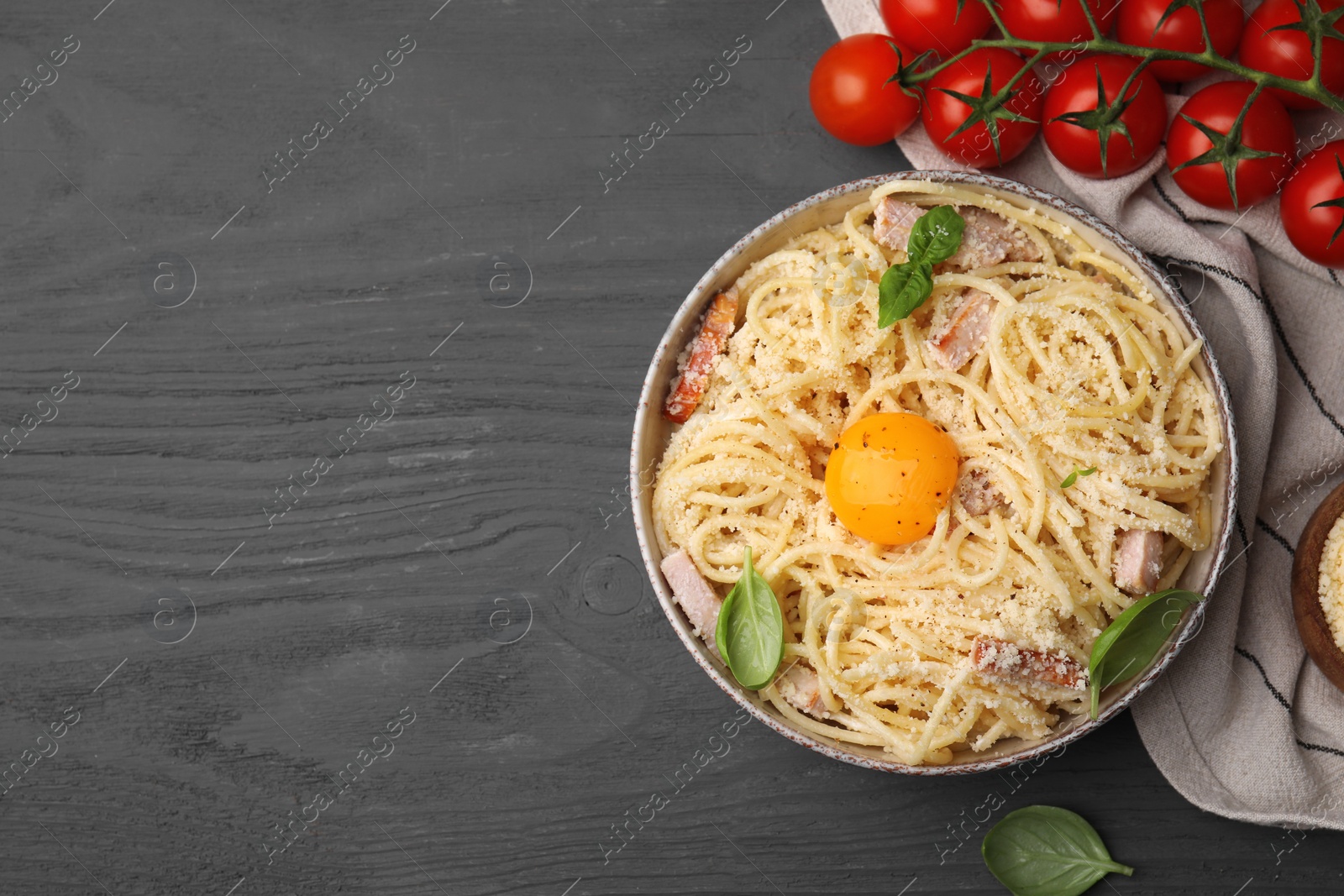Photo of Bowl of tasty pasta Carbonara with egg yolk on grey wooden table, flat lay. Space for text