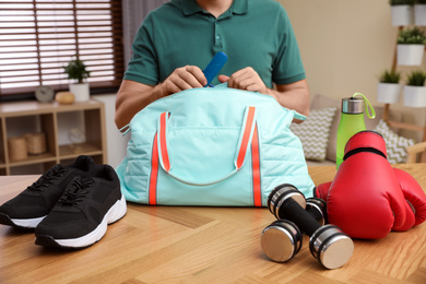 Photo of Man packing sports bag for training indoors, closeup