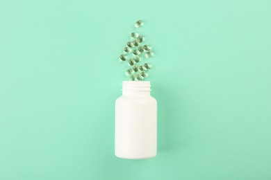 Bottle and vitamin capsules on turquoise background, top view