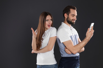 Indignant young woman looking into boyfriend's smartphone on black background. Relationship problems