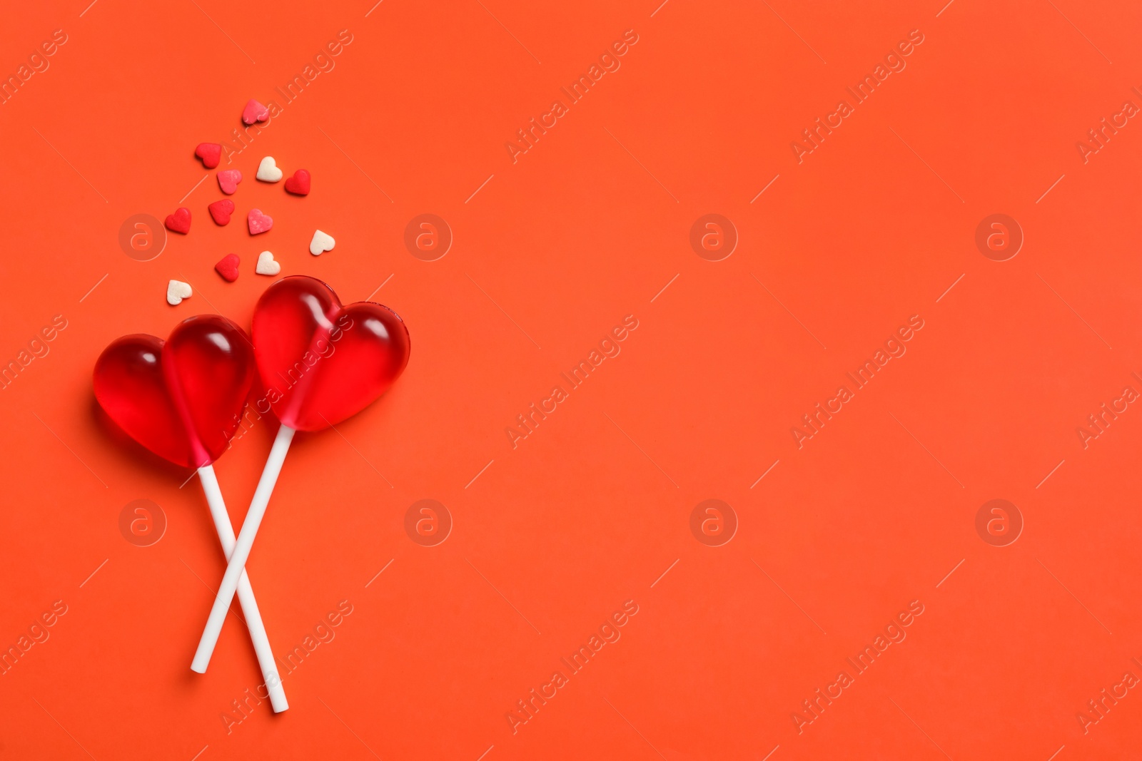 Photo of Sweet heart shaped lollipops and sprinkles on coral background, flat lay with space for text. Valentine's day celebration