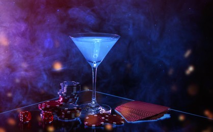 Image of Casino chips, dice, playing cards and cocktail on dark background with smoke