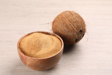 Photo of Coconut sugar in bowl and fruit on light wooden table, closeup