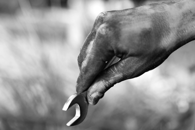 Dirty worker holding wrench on blurred background, closeup of hand. Black and white effect