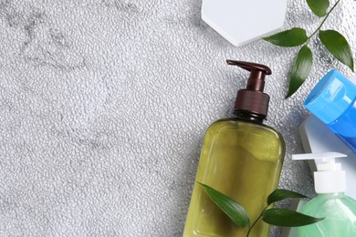 Photo of Different face cleansing products and green leaves on white textured table, flat lay. Space for text