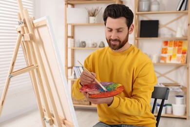 Photo of Man painting in studio. Using easel to hold canvas