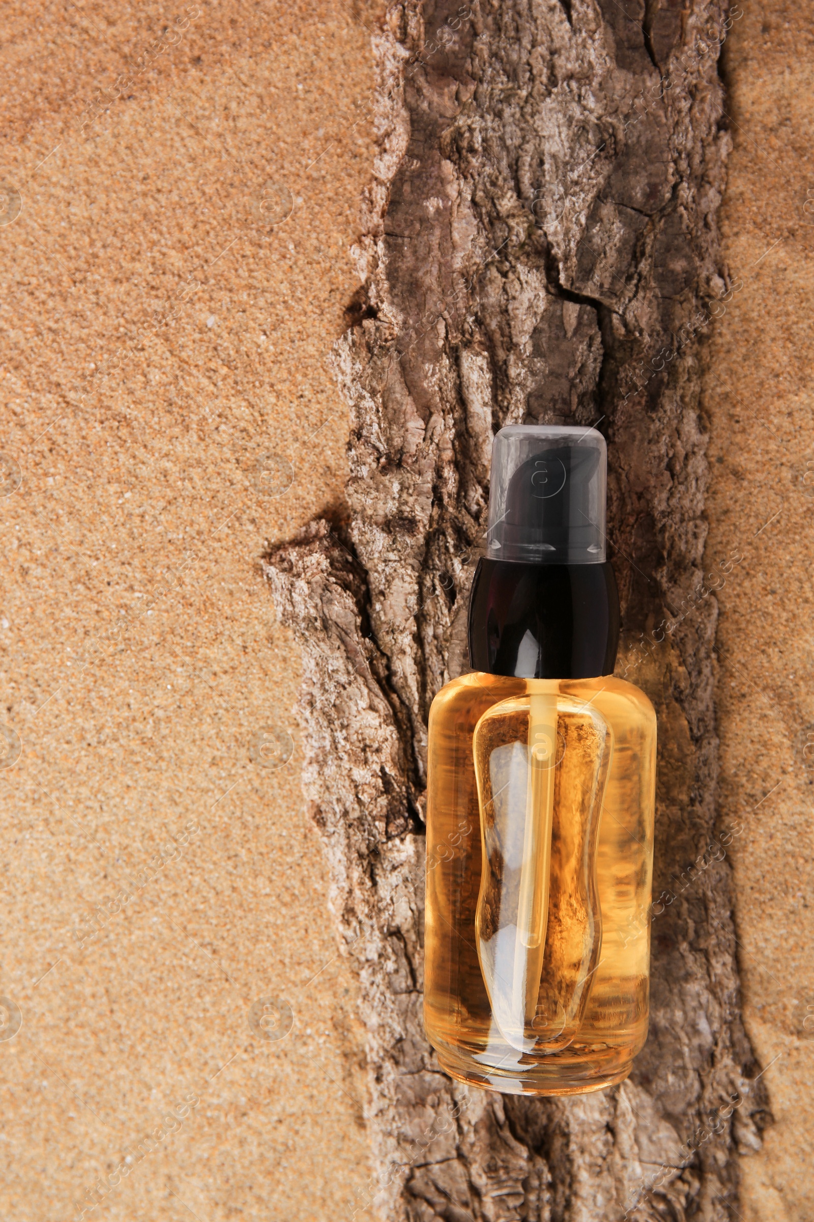 Photo of Bottle of serum and tree bark on sand, top view