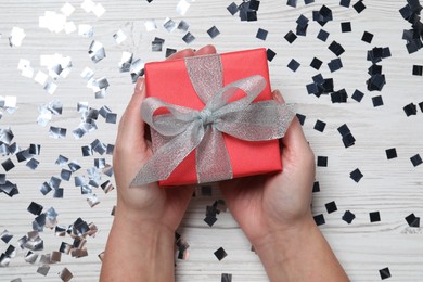 Photo of Christmas present. Woman with gift box and confetti on white wooden background, top view