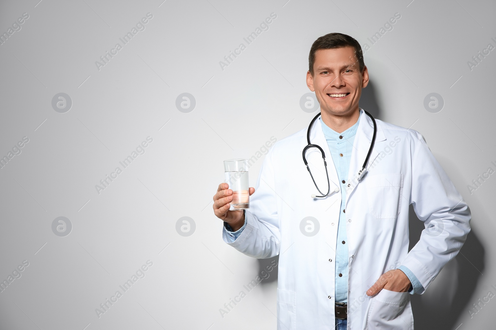 Photo of Nutritionist holding glass of pure water on light grey background. Space for text