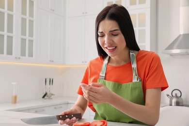 Photo of Young woman cutting finger with knife while cooking in kitchen. Space for text