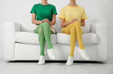 Women wearing bright tights sitting on sofa indoors, closeup