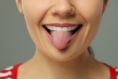 Photo of Happy young woman showing her tongue on grey background, closeup