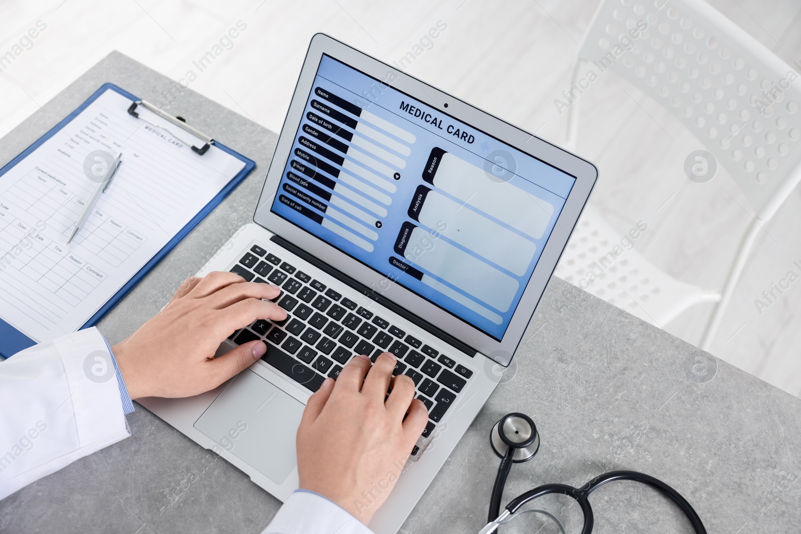 Photo of Doctor using laptop to fill out patient's medical card at table in clinic, closeup