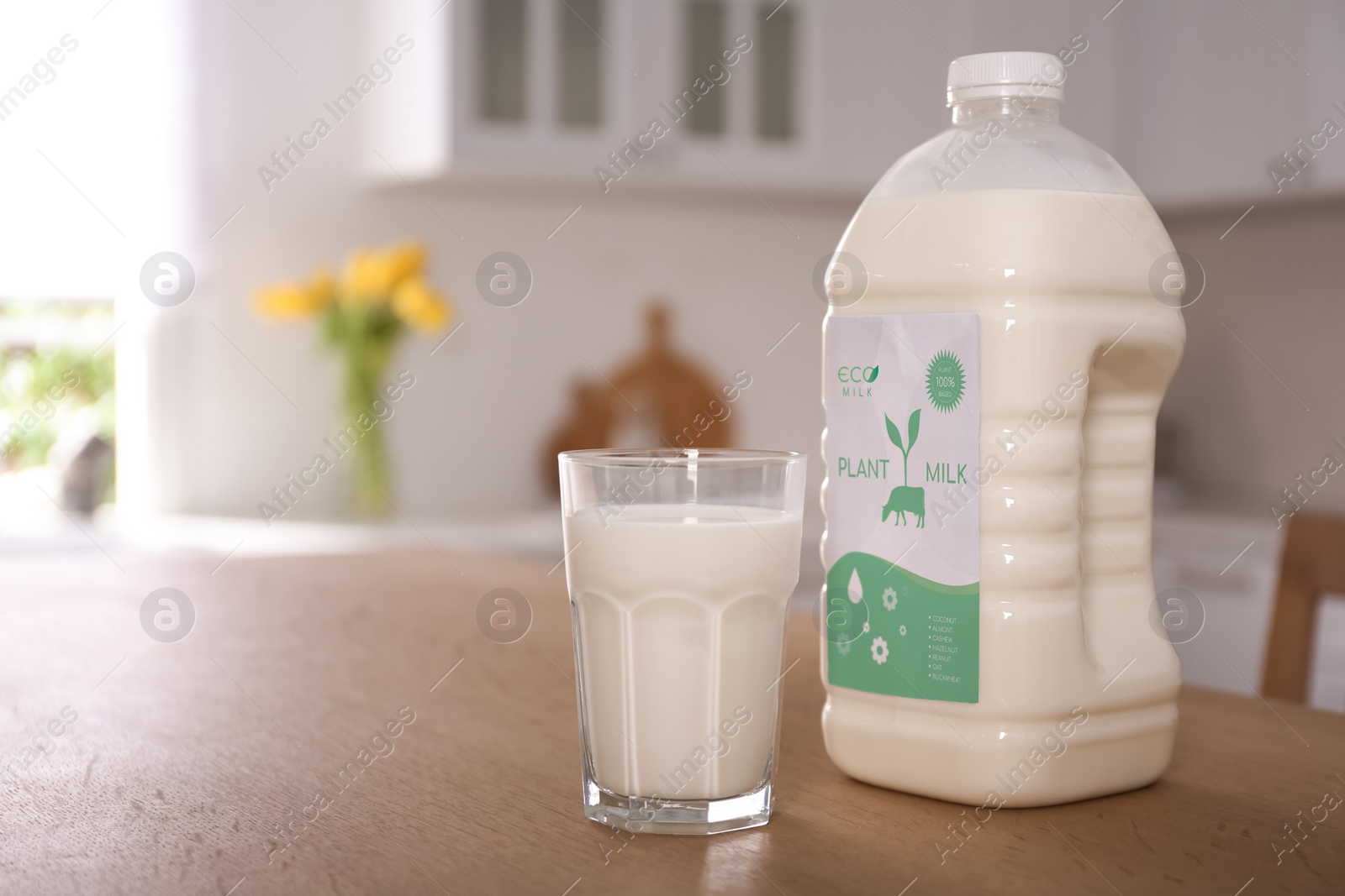 Image of Gallon bottle and glass of vegan milk on wooden table in kitchen. Space for text