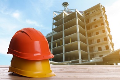 Safety equipment. Hard hats on wooden surface near unfinished building outdoors, space for text