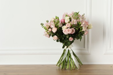 Photo of Beautiful bouquet of fresh flowers on wooden table near white wall, space for text