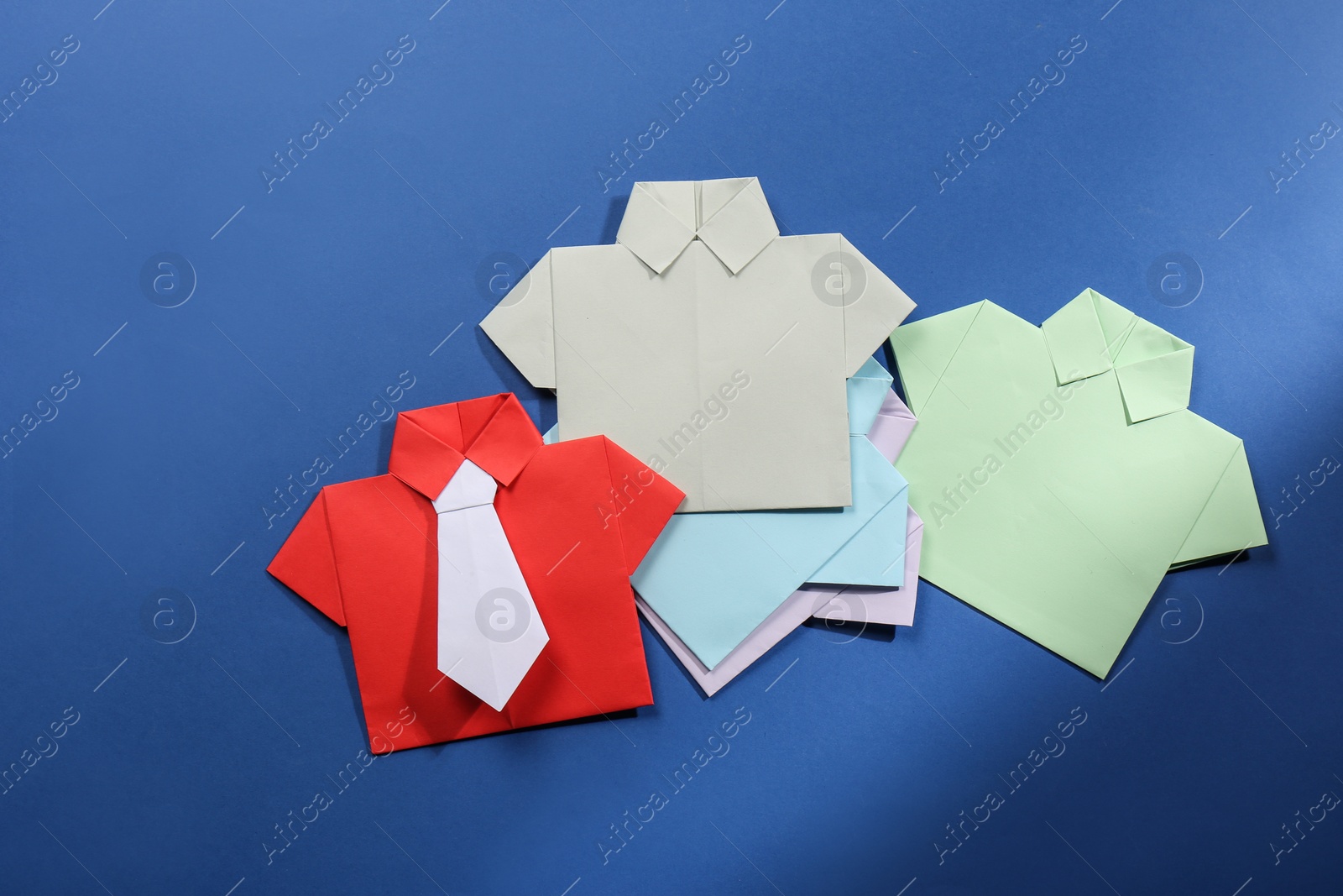 Photo of Many paper shirts on blue background, flat lay. Recruiter searching employee