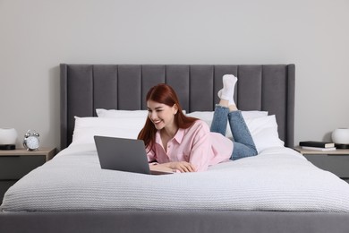 Happy woman with laptop on bed in bedroom