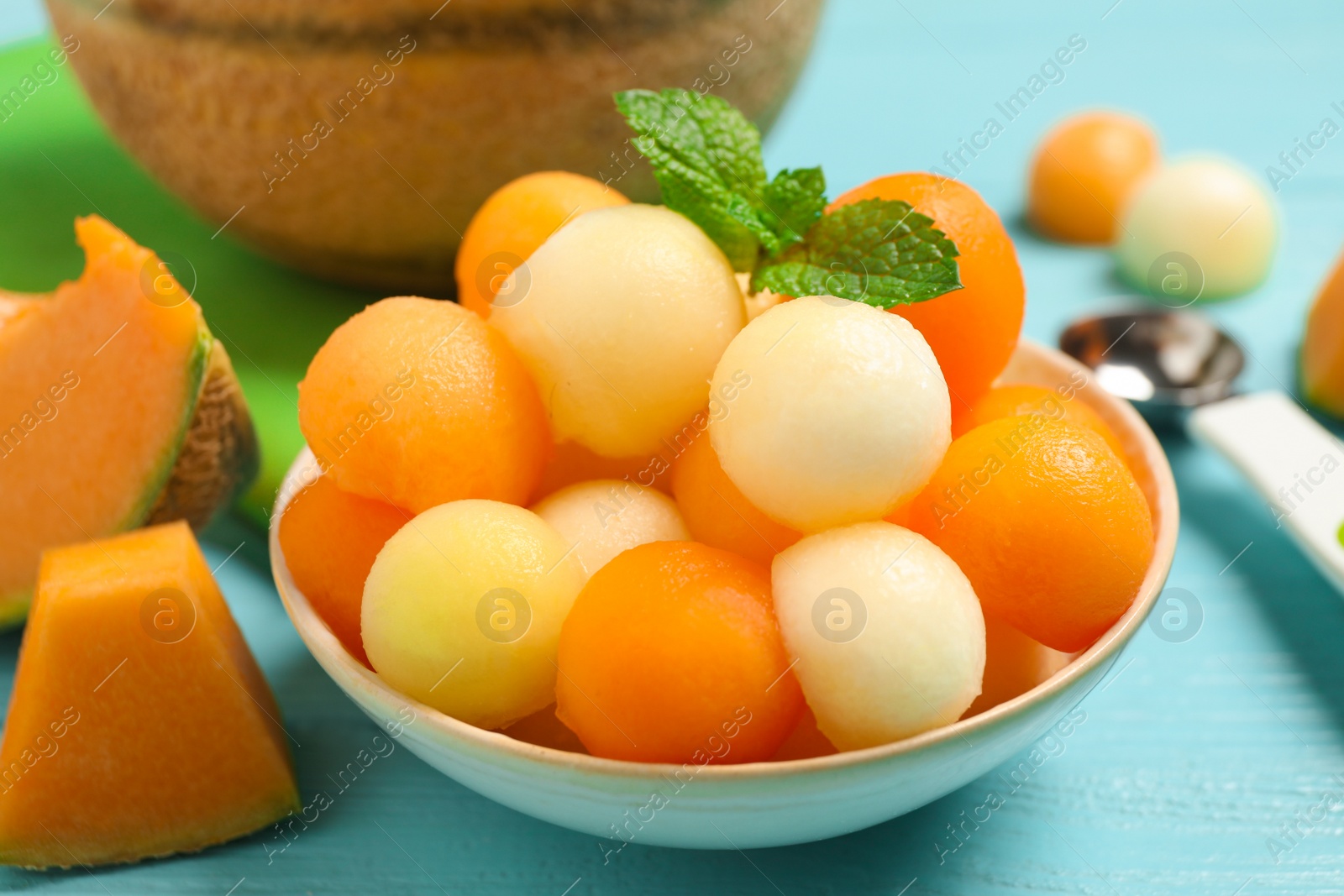 Photo of Melon balls and mint in bowl on light blue table, closeup
