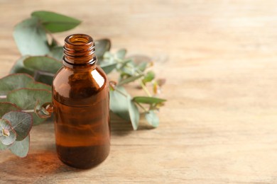 Photo of Bottle of eucalyptus essential oil and leaves on wooden table. Space for text