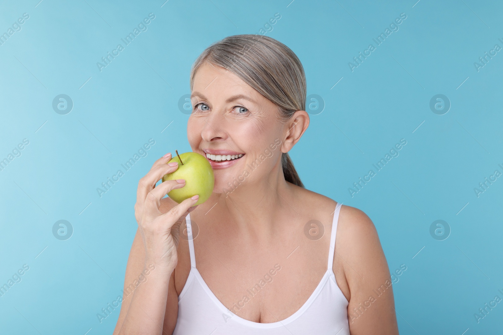 Photo of Beautiful woman with fresh apple on light blue background. Vitamin rich food