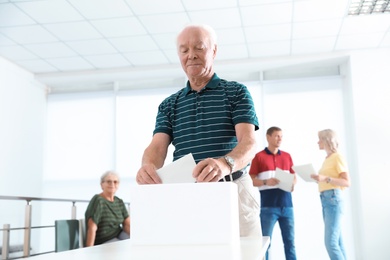 Photo of Elderly man putting ballot paper into box at polling station